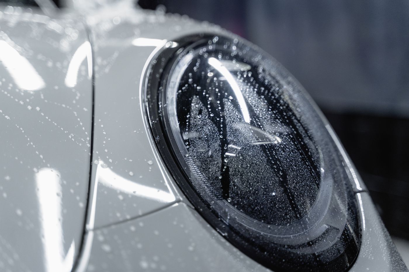 Water beads on a glossy silver car headlight and fender
